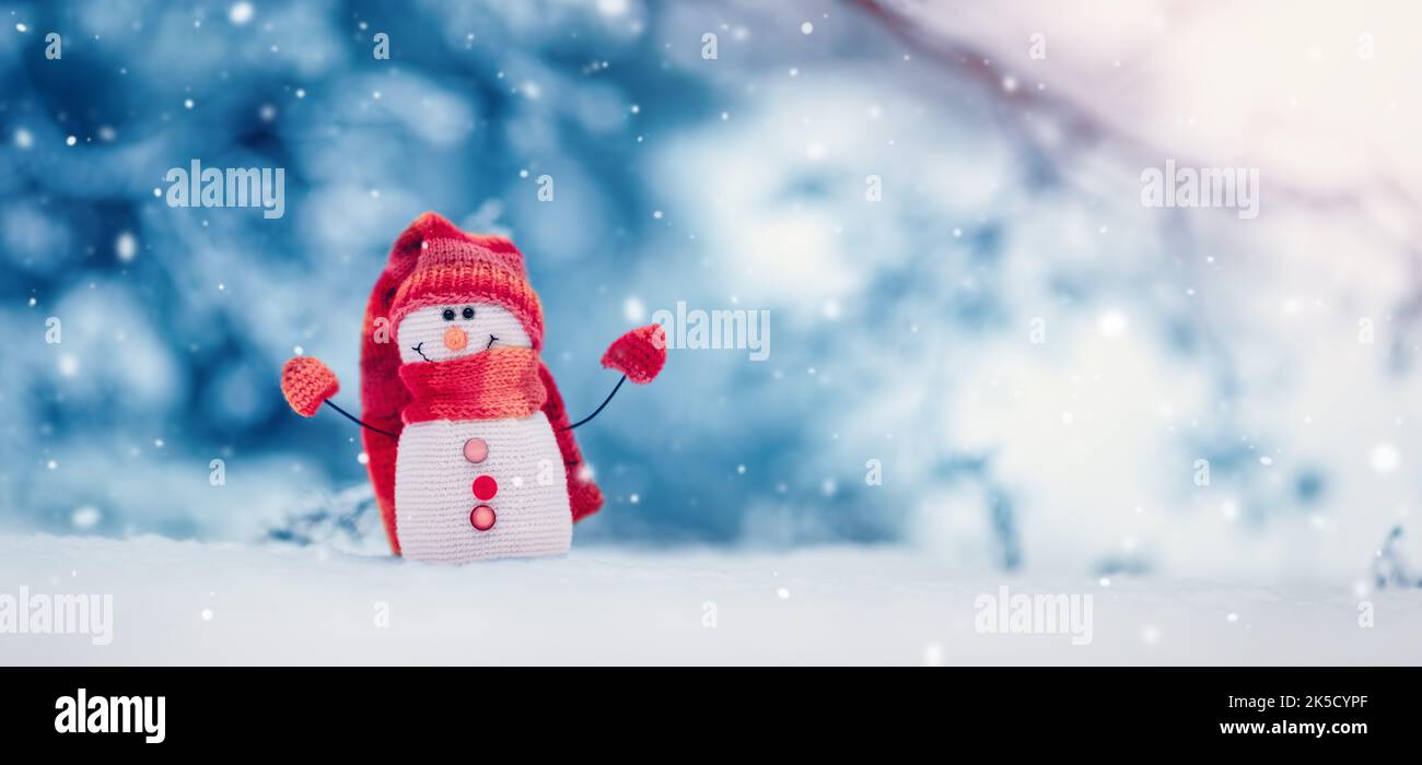 Piccolo pupazzo di neve lavorato a maglia sulla neve bianca su sfondo blu. Foto Stock