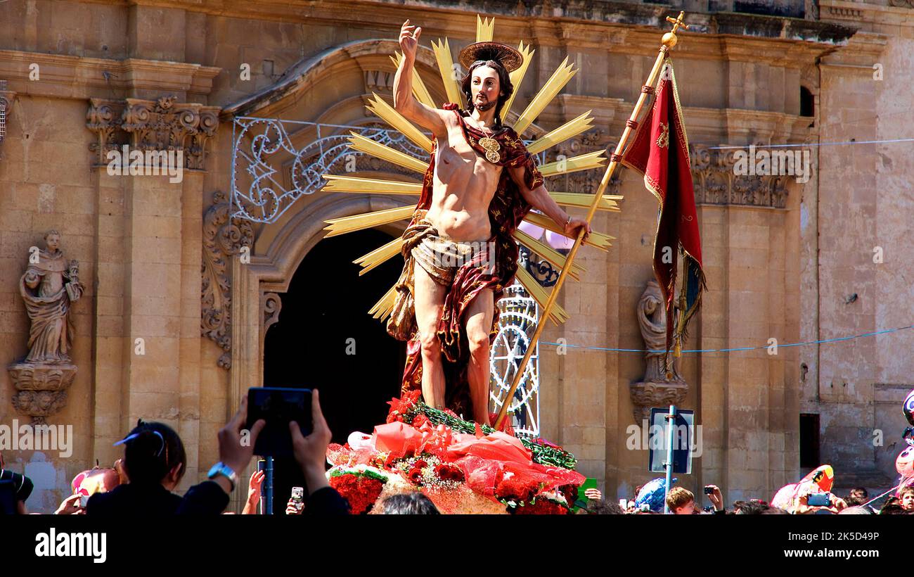 Italia, Sicilia, angolo barocco, città barocca Scigli, Domenica di Pasqua, Statua di Cristo risorto è portato su piedistallo in processione attraverso la città, alone intorno a Cristo, bandiera, chiesa sullo sfondo, folla, fotografi Foto Stock