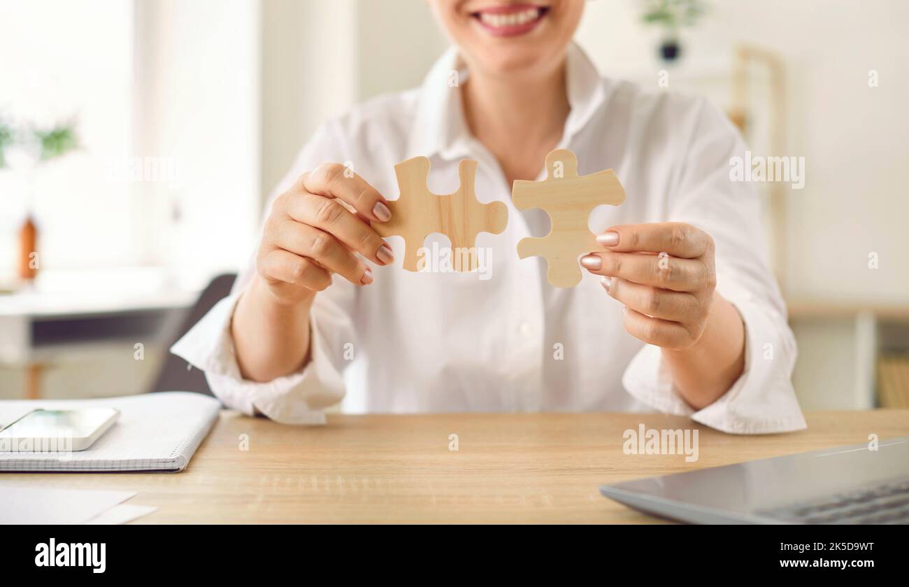 Primo piano di due pezzi di legno puzzle in mani di irriconoscibile sorridente donna d'affari. Foto Stock