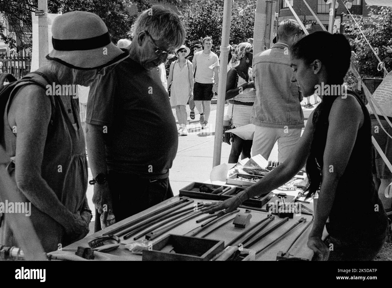 Un artigiano mostra i suoi archi di violino fatti a mano ai clienti al Lowell Folk Festival nella storica Lowell, Massachusetts. L'immagine è stata acquisita in nero Foto Stock