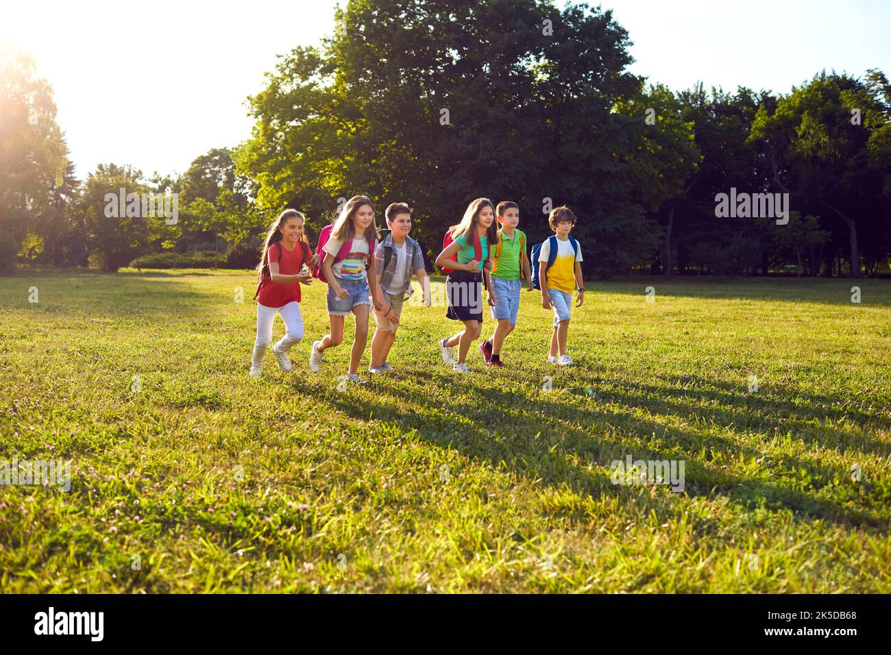 Un gruppo felice di scolari si diverte nella natura all'aperto nel parco durante una giornata di sole calde. Foto Stock