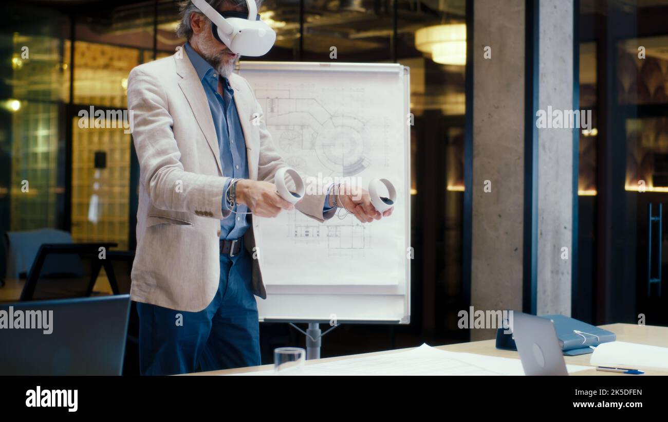 Ingegnere maschile che utilizza controller wireless, gesturing, esaminando il progetto dalla lavagna a fogli mobili in realtà virtuale, guardando i dati, lavorando in un ufficio moderno di un'azienda hi-tech. Tecnologia digitale nel cyberspazio. Foto Stock