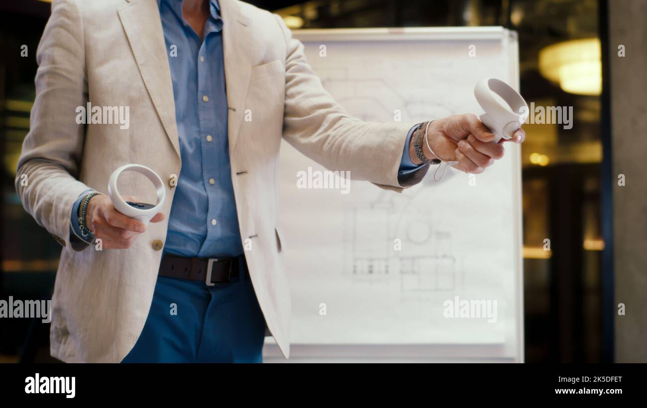 Ingegnere maschile che utilizza controller wireless, gesturing, esaminando il progetto dalla lavagna a fogli mobili in realtà virtuale, guardando i dati, lavorando in un ufficio moderno di un'azienda hi-tech. Tecnologia digitale nel cyberspazio. Foto Stock