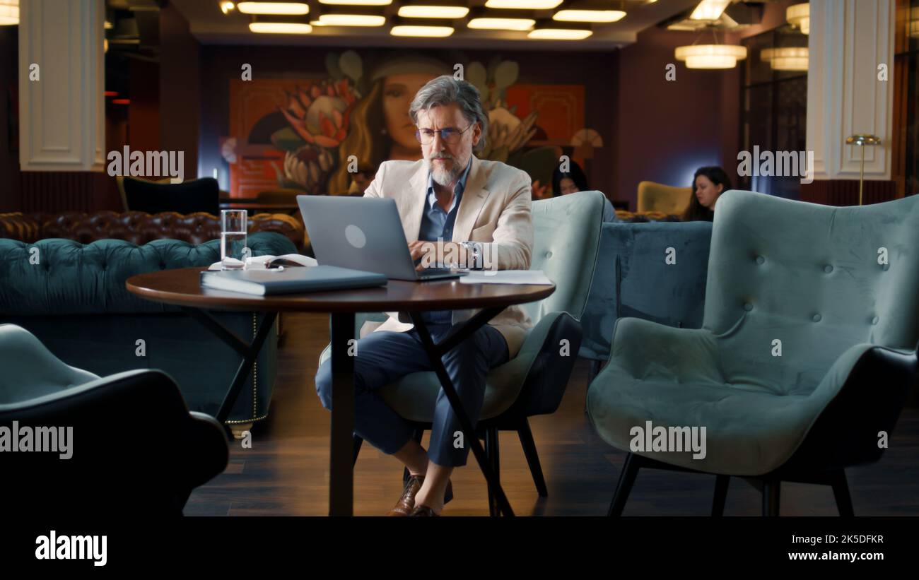 Uomo d'affari maturo che usa il laptop, che lavora in linea sul progetto di startup, strategia di affari, che analizza i documenti e i documenti in Office cafè. Lavoratore di e-commercio che commercializza l'azienda Foto Stock