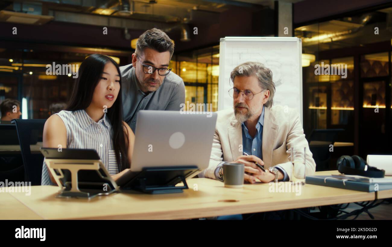 Team multietnico di lavoratori creativi che discutono di strategia aziendale o progetto di startup in un ufficio moderno utilizzando un computer portatile. Società di e-commerce. Lavorare sul progetto di avvio Foto Stock