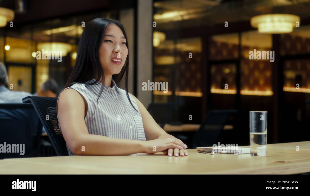 Donna asiatica che parla online con il cliente, avendo videochiamata, lavorando in un moderno ufficio di società di marketing. Riunione virtuale di affari. Pubblicità e vendita di prodotti Foto Stock