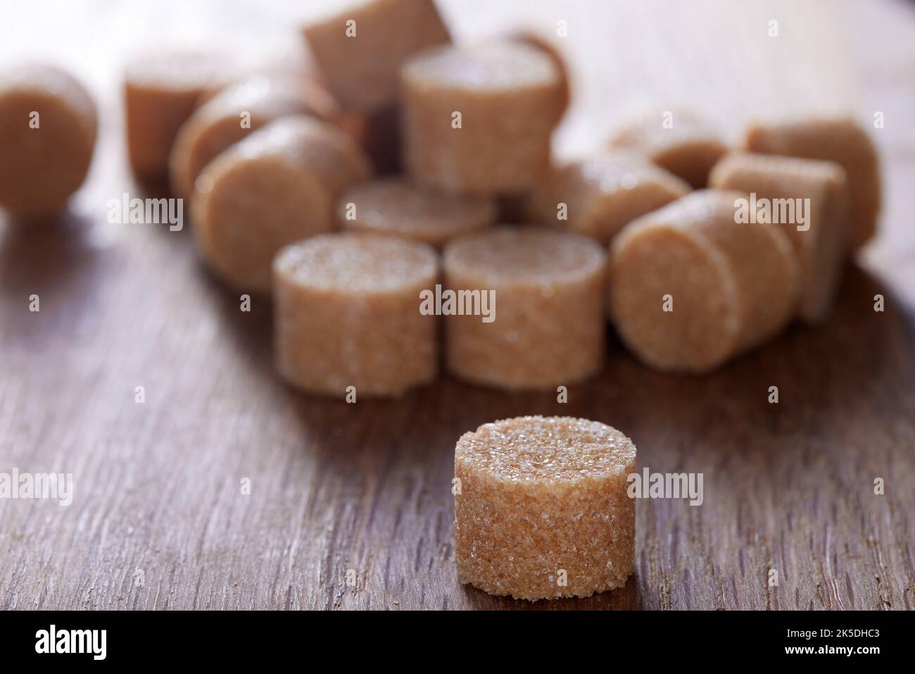 Lo zucchero rotondo marrone si forma su un vecchio tagliere di legno scuro - vista ravvicinata Foto Stock