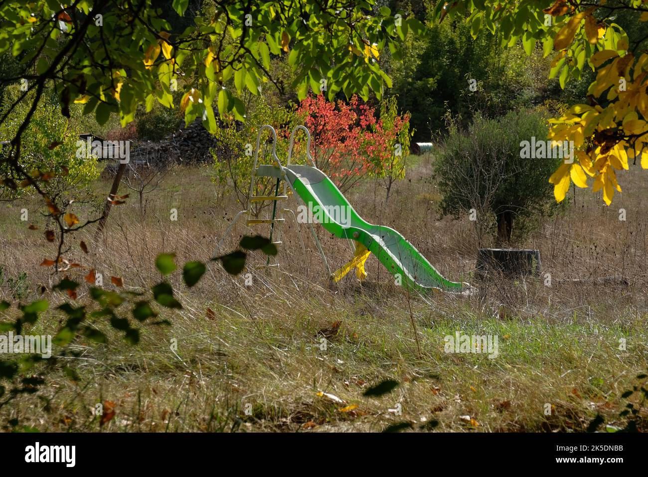 Aude France 10.6.22 lo scivolo in plastica verde per bambini è stato dimenticato in un giardino troppo grande. Erba alta inclinata. Foglie autunnali. Arbusti e alberi. Foto Stock