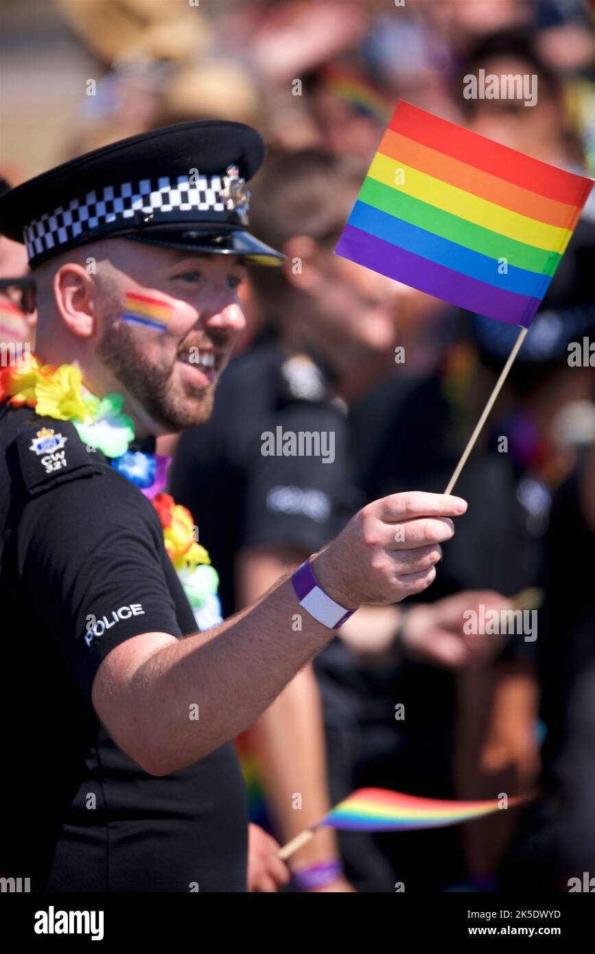 Brighton & Hove Pride Festival, Brighton & Hove, East Sussex, Inghilterra. Poliziotto britannico in uniforme con bandiera arcobaleno dipinta sul viso e in mano Foto Stock