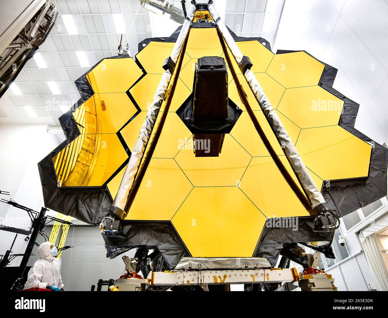 James Webb Space Telescope (JWST) Primary Mirror preparato per test all'interno di una camera bianca presso il Johnson Space Center della NASA a Houston, dove subirà l'ultimo test criogenico prima che venga lanciato nello spazio. In preparazione alla prova, le ali dello specchio (che sono costituite dai tre segmenti su ciascun lato) sono state aperte. Questa foto mostra un'ala completamente estratta e un'ala a pochi istanti dall'implementazione completa. Un ingegnere osserva. Una versione ottimizzata di un'immagine NASA di Chris Gunn, un fotografo esperto. Credito: NASA/Chris Gunn. Solo per uso editoriale. Foto Stock