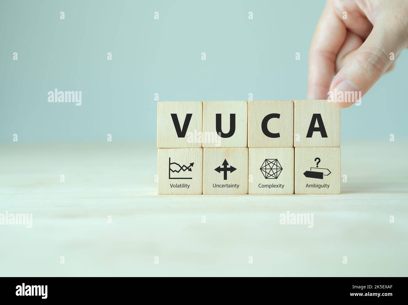 VUCA e gestione strategica. Cubi di legno con icona e testo VUCA; volatilità, incertezza, complessità, ambiguità con sfondo grigio. Gestione intelligente Foto Stock