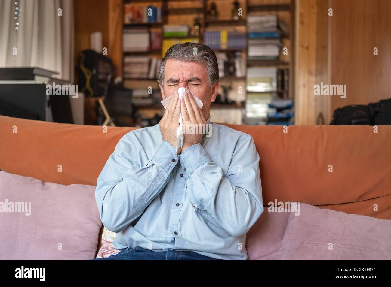 Malato di influenza e starnuti in un tessuto, seduto a casa. Foto Stock