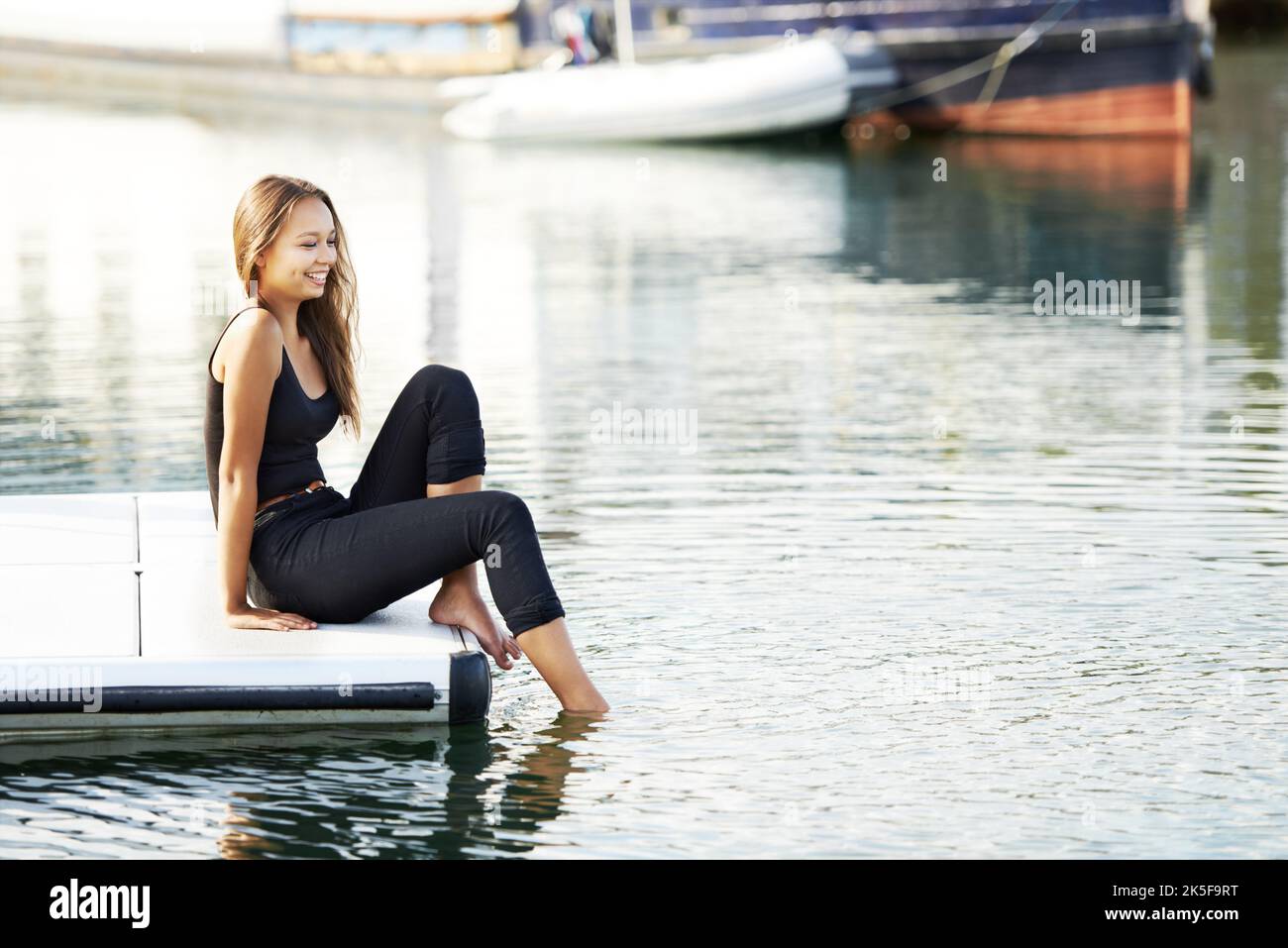 Test dell'acqua. Una bellissima giovane donna seduta con i piedi in acqua al porto. Foto Stock