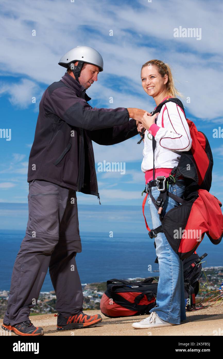 Esecuzione di un controllo di sicurezza rapido. Un parapendio sorridendo come la sua istruttore le aiuta a stringere le cinghie. Foto Stock