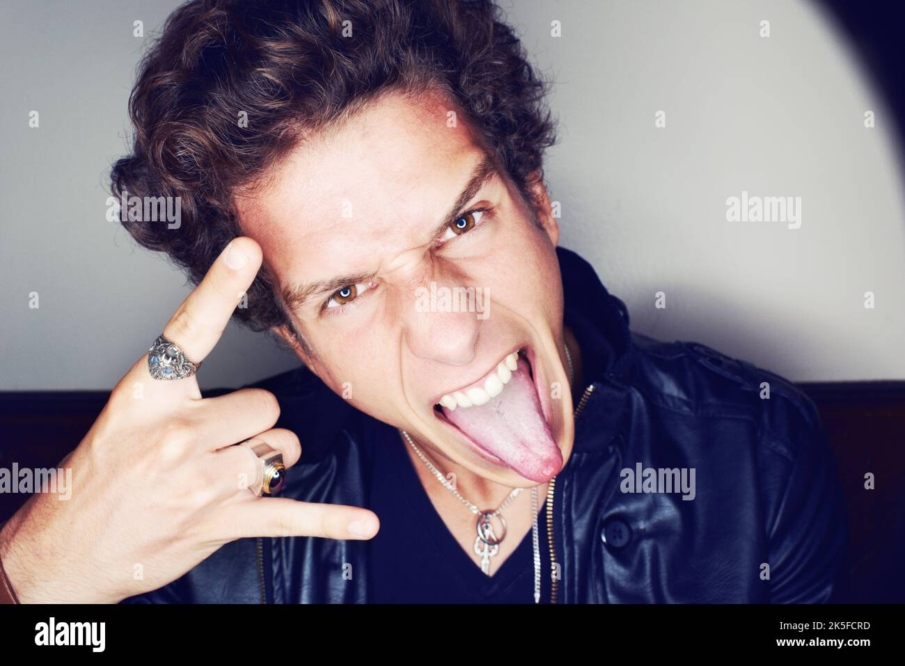 Rock n Roll. Primo piano ritratto di un giovane uomo che attacca la lingua e fa gesti di mano circondati da un alone di luce. Foto Stock