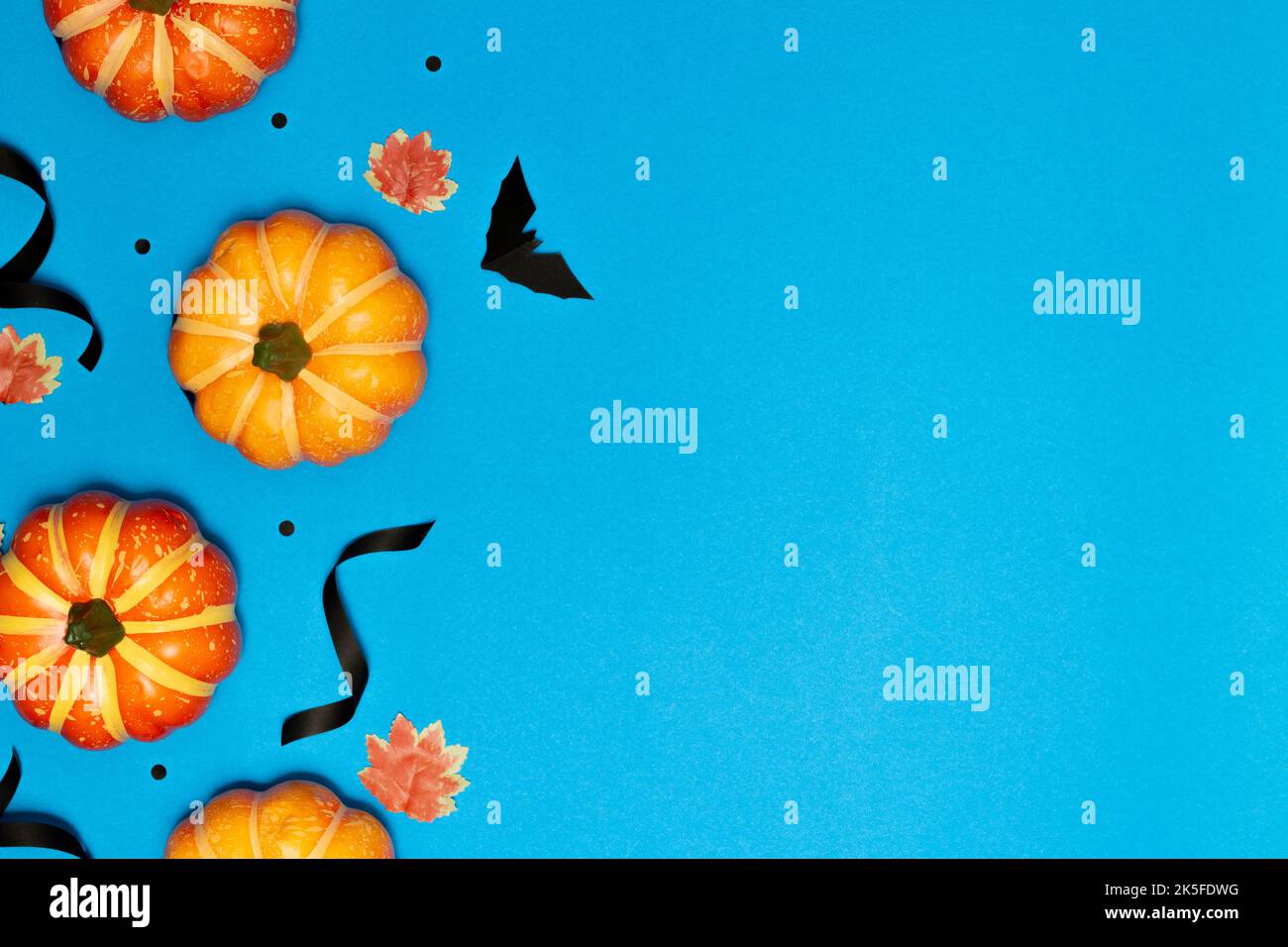 Concetto di Halloween, sorriso spaventoso zucca e pipistrello nero con foglie di acero su sfondo azzurro. Foto Stock