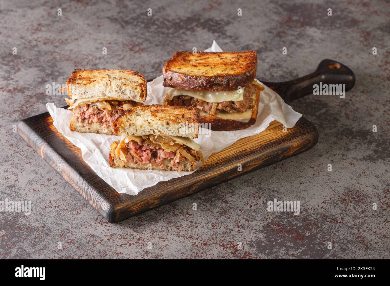 Il sandwich patty Melt ha un hamburger coperto con formaggio svizzero fuso, cipolle caramellate e fette di pane di segale griddled closeup sul bo di legno Foto Stock