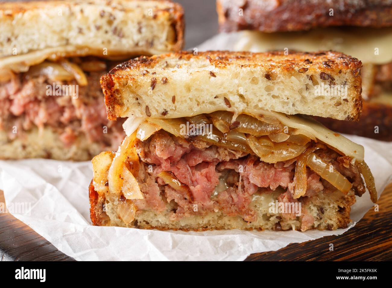 Sandwich Patty Melt costituito da uno strato di cipolle caramellate, formaggio e hamburger patty tra il pane tostato primo piano sul pannello di legno sul tavolo. H Foto Stock