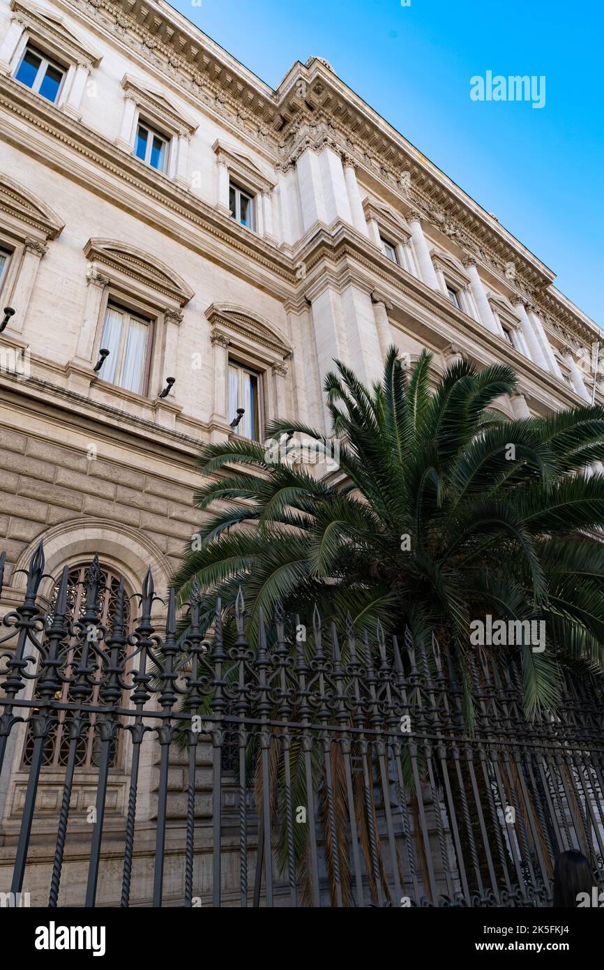 Elegante facciata neoclassica del palazzo romano con colonne ornate e palme dietro ringhiere in ferro battuto Foto Stock