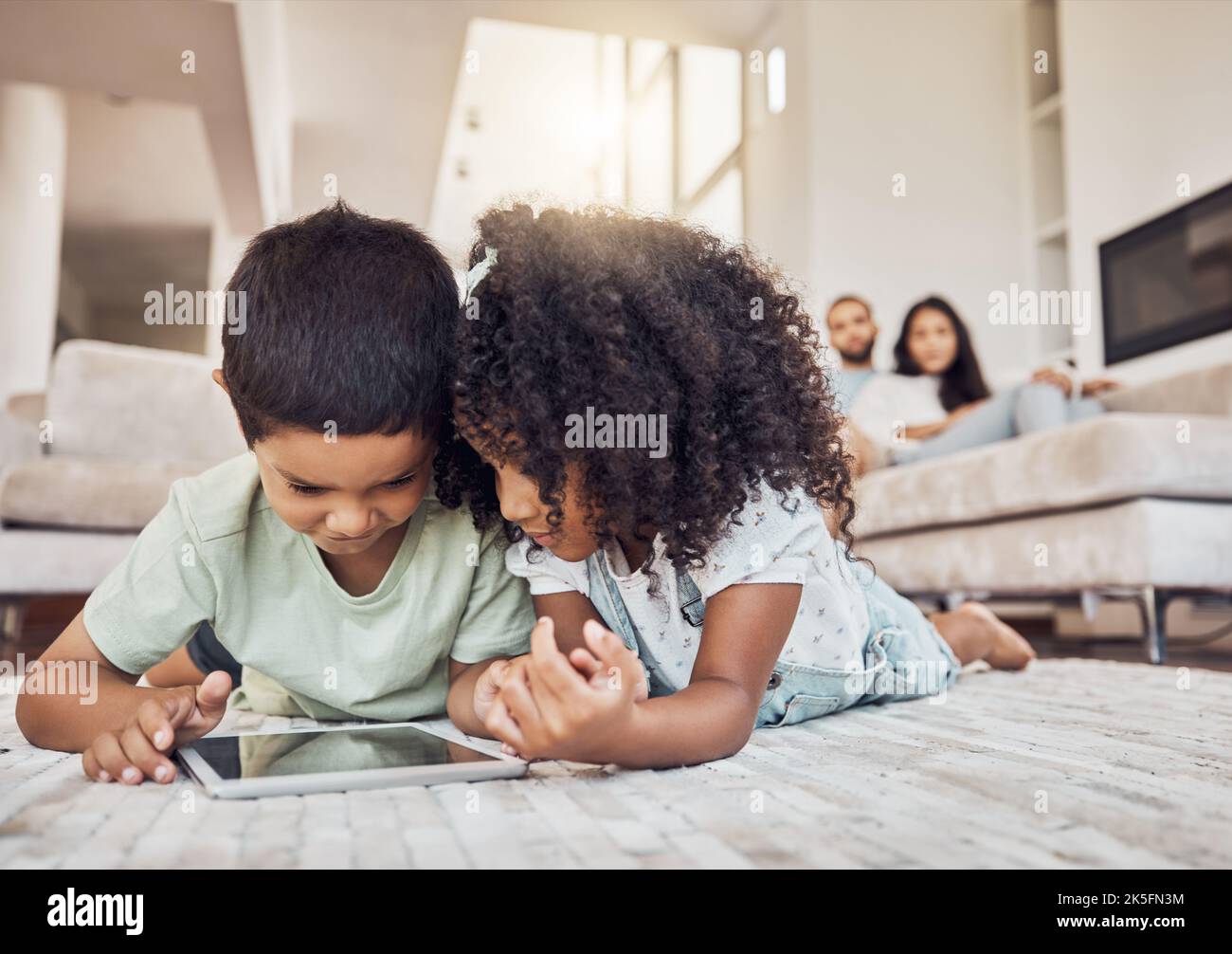 I bambini, il fratello e la sorella sul tablet guardano, imparano o trasmettono in streaming video educativi, giochi o cartoni animati sul tappeto della lounge a casa. Bambini che giocano Foto Stock