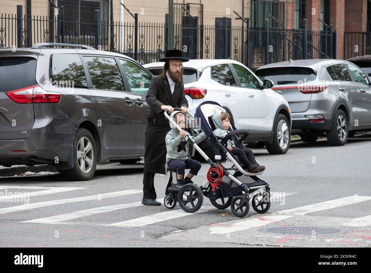 Un padre ebreo ortodosso con 2 bambini in passeggino per 2. Su Bedford Avenue a Williamsburg, Brooklyn, New York City. Foto Stock