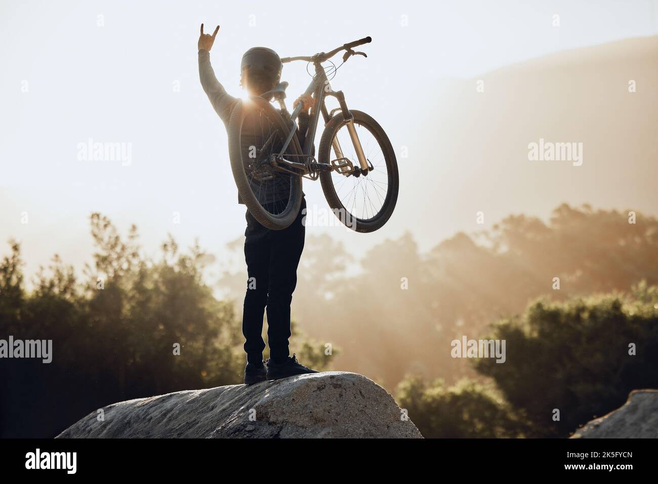 Mountain bike, avventura e vincitore uomo con rock, successo o festeggiamenti segno e bicicletta per la concorrenza all'aperto. Una persona che viaggia in moto festeggia Foto Stock