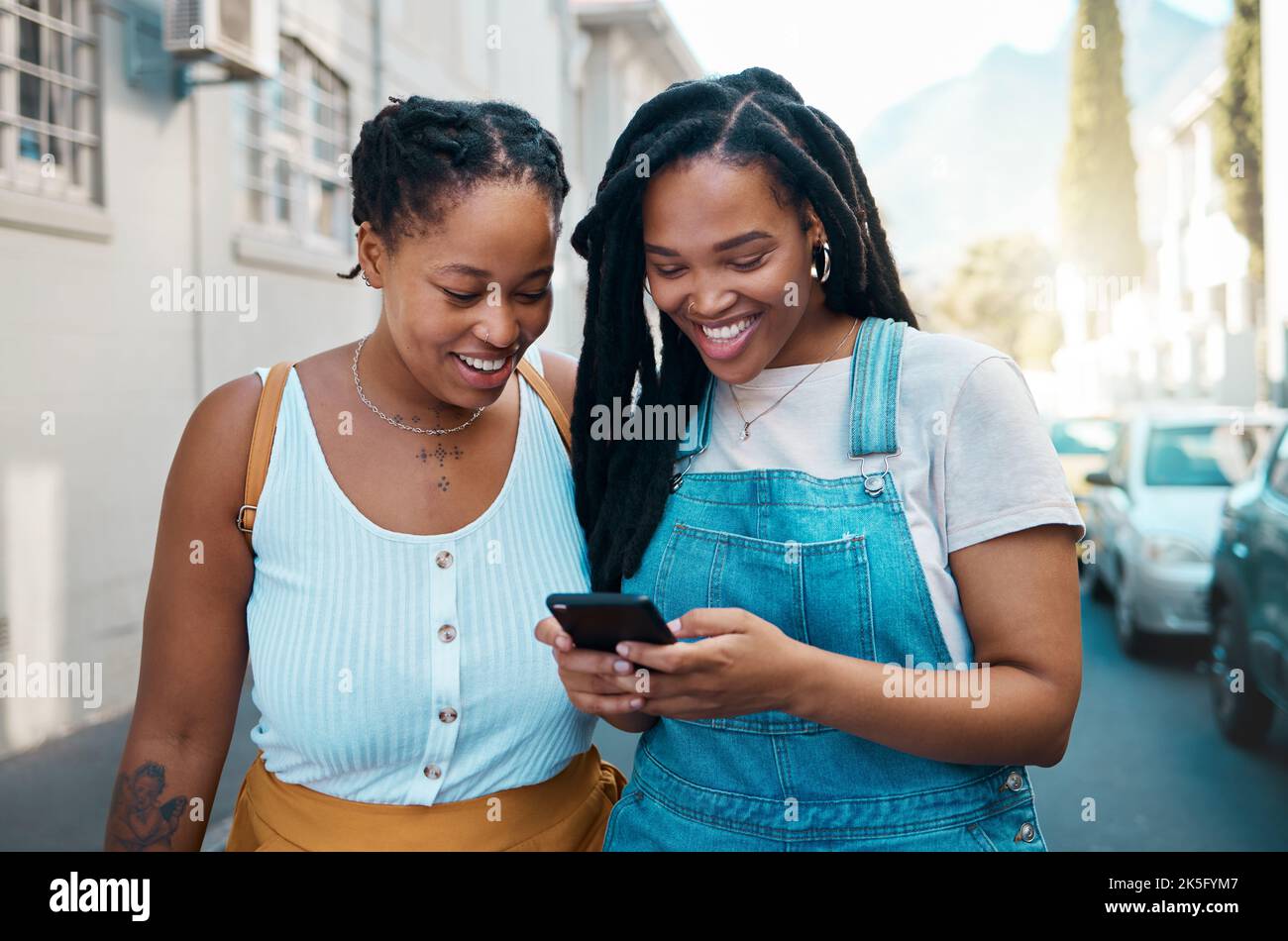 Felice donna nera, amici e telefono in comunicazione di social media, SMS insieme fuori una strada urbana. Donne africane sorridenti per 5G connessione Foto Stock