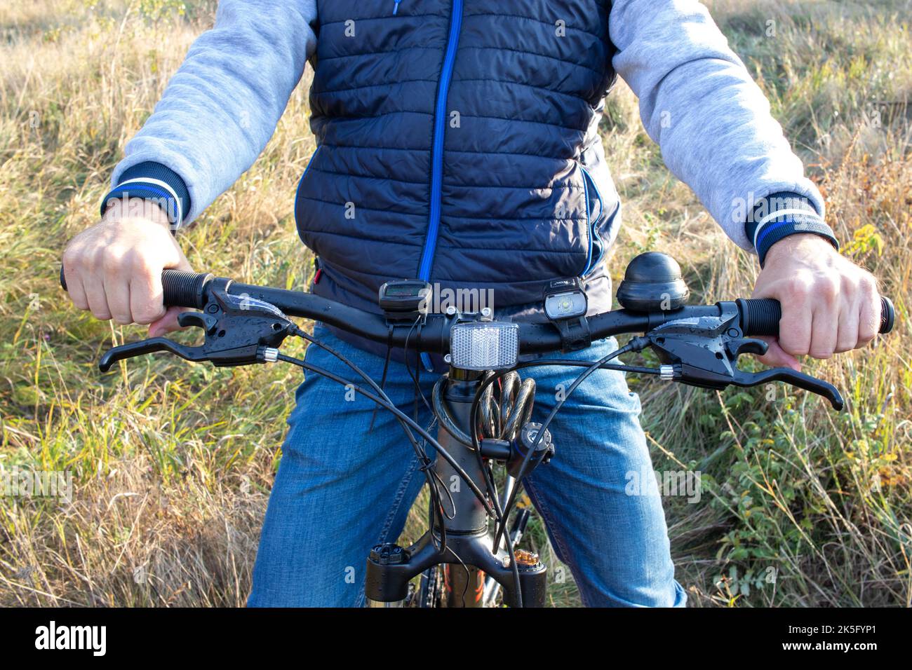 Persona in bicicletta. Un uomo tiene il manubrio di una bicicletta su sfondo erboso su un campo. Primo piano Foto Stock