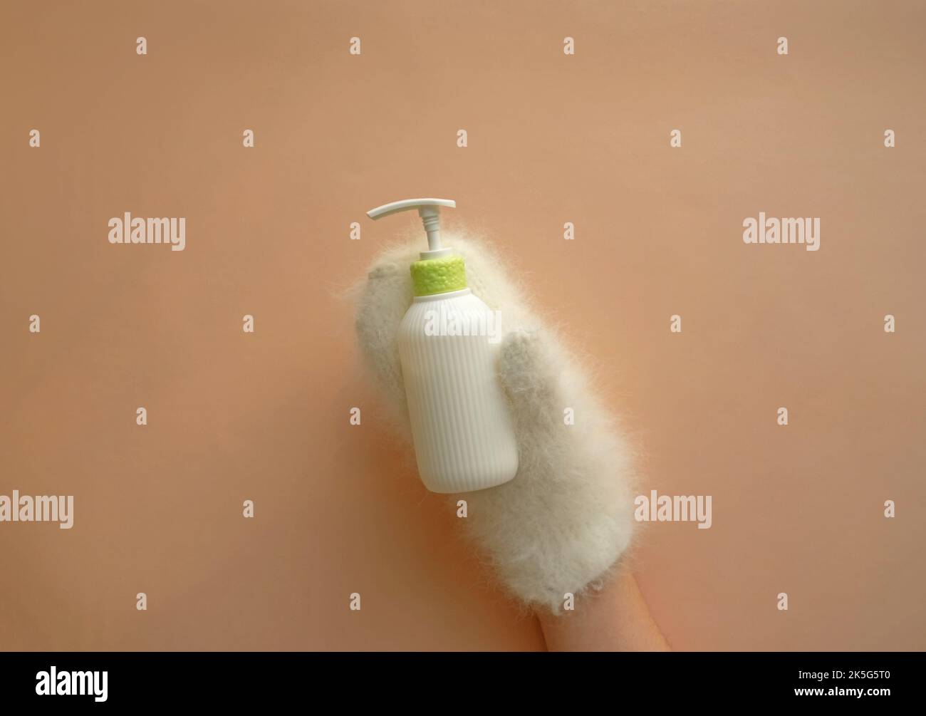 La bottiglia cosmetica della lozione idratante tiene le mani nei mitens. Foto Stock