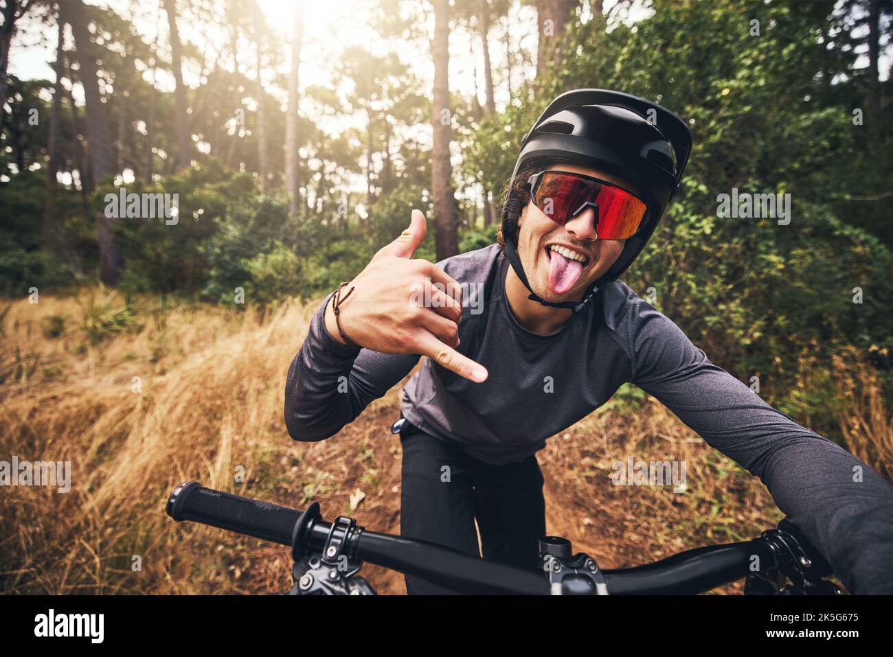 Mountain bike, ciclismo e fitness con un gesto uomo un segno shaka mano durante l'allenamento o l'esercizio nella natura del Brasile. Ritratto di un maschio professionista Foto Stock
