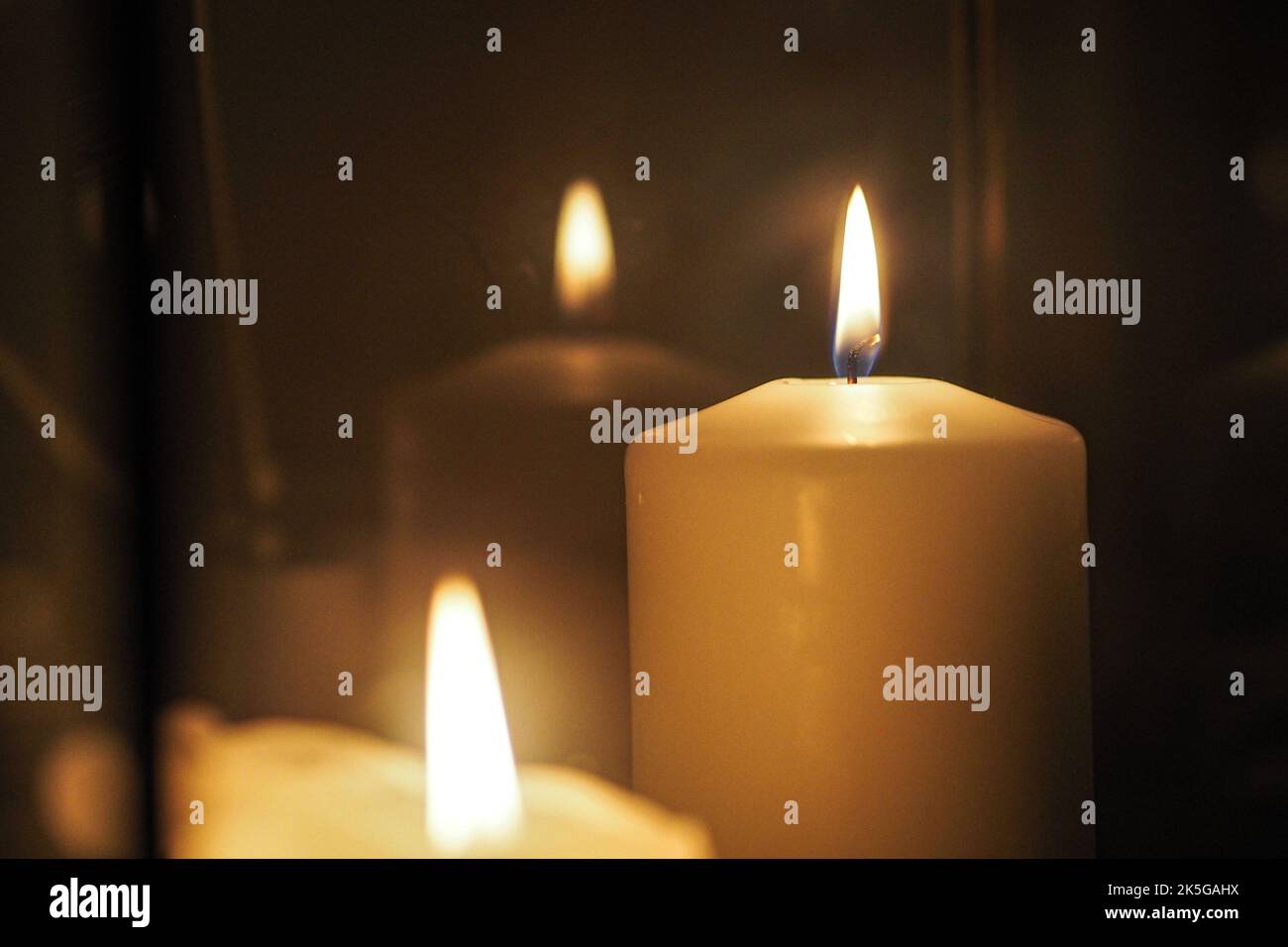 Un primo piano di candele accese riflesse in un portacandele geometrico in filo metallico in una stanza buia Foto Stock