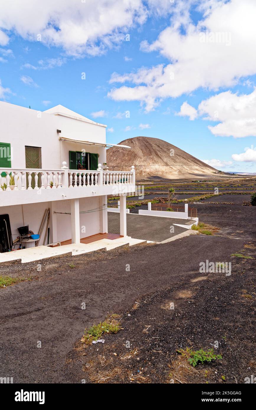 Tipica casa colonica bianca delle Canarie sull'isola di Lanzarote a Mancha Blanca con crateri vulcanici sullo sfondo in un soleggiato pomeriggio invernale. Lanzarote è Foto Stock