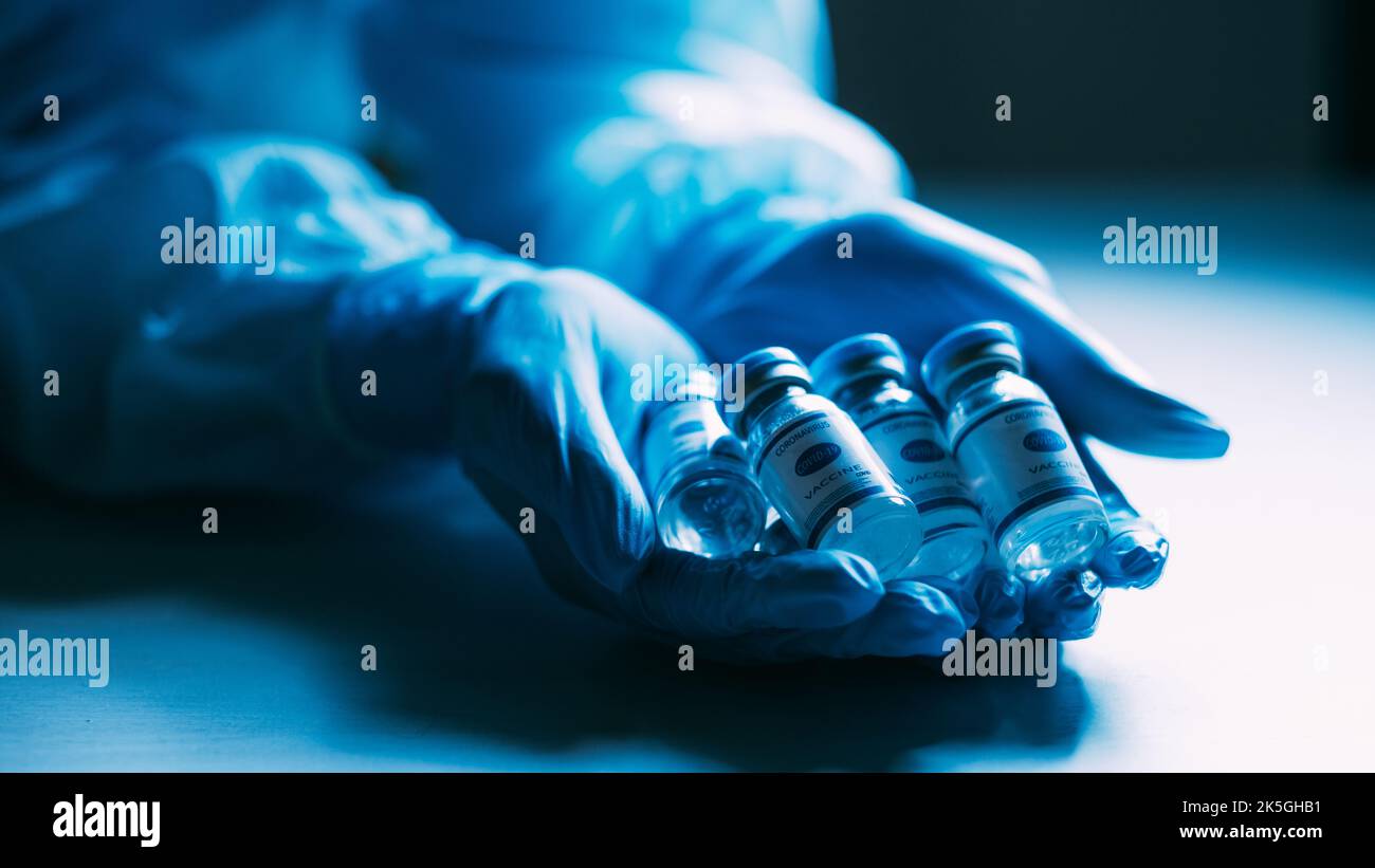 Sviluppo di vaccini. Immunizzazione con Covid-19. Inoculazione pandemica. Trattamento medico. Flaconi dosatori flaconi con etichetta nelle mani del medico in blu protec Foto Stock