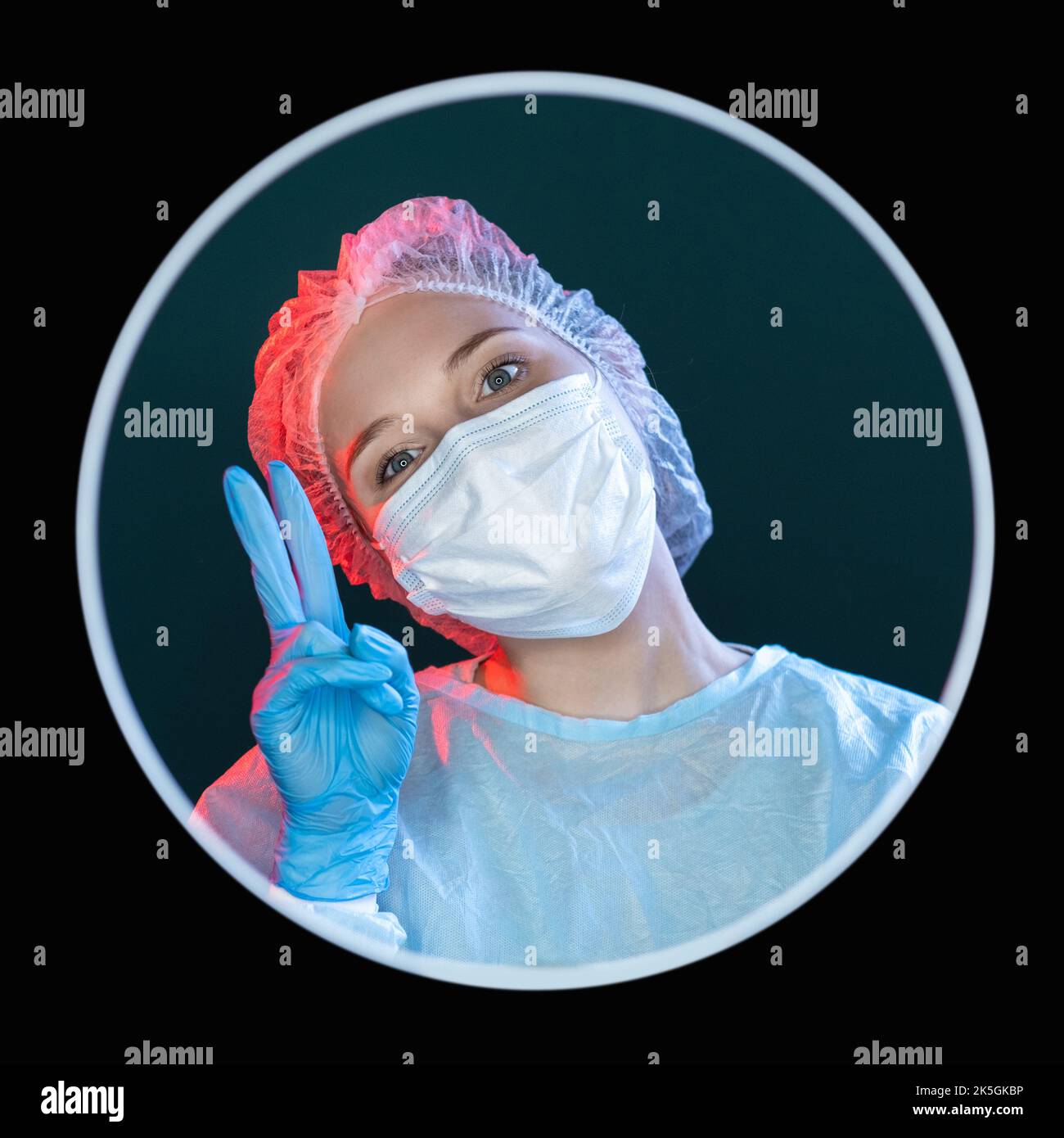 Dottore ottimista. Segno di pace. Assistenza medica. Ritratto di positiva femmina infermiera felice in blu dpi maschera guanti mostrando vittoria due dita V gesto Foto Stock