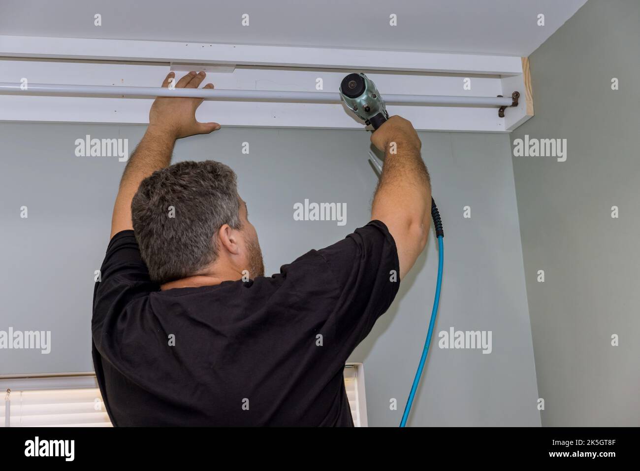 Un handyman professionale sta inchiodando i cornicioni di legno sulla parete della tenda sopra la finestra della sede recentemente costruita. Foto Stock