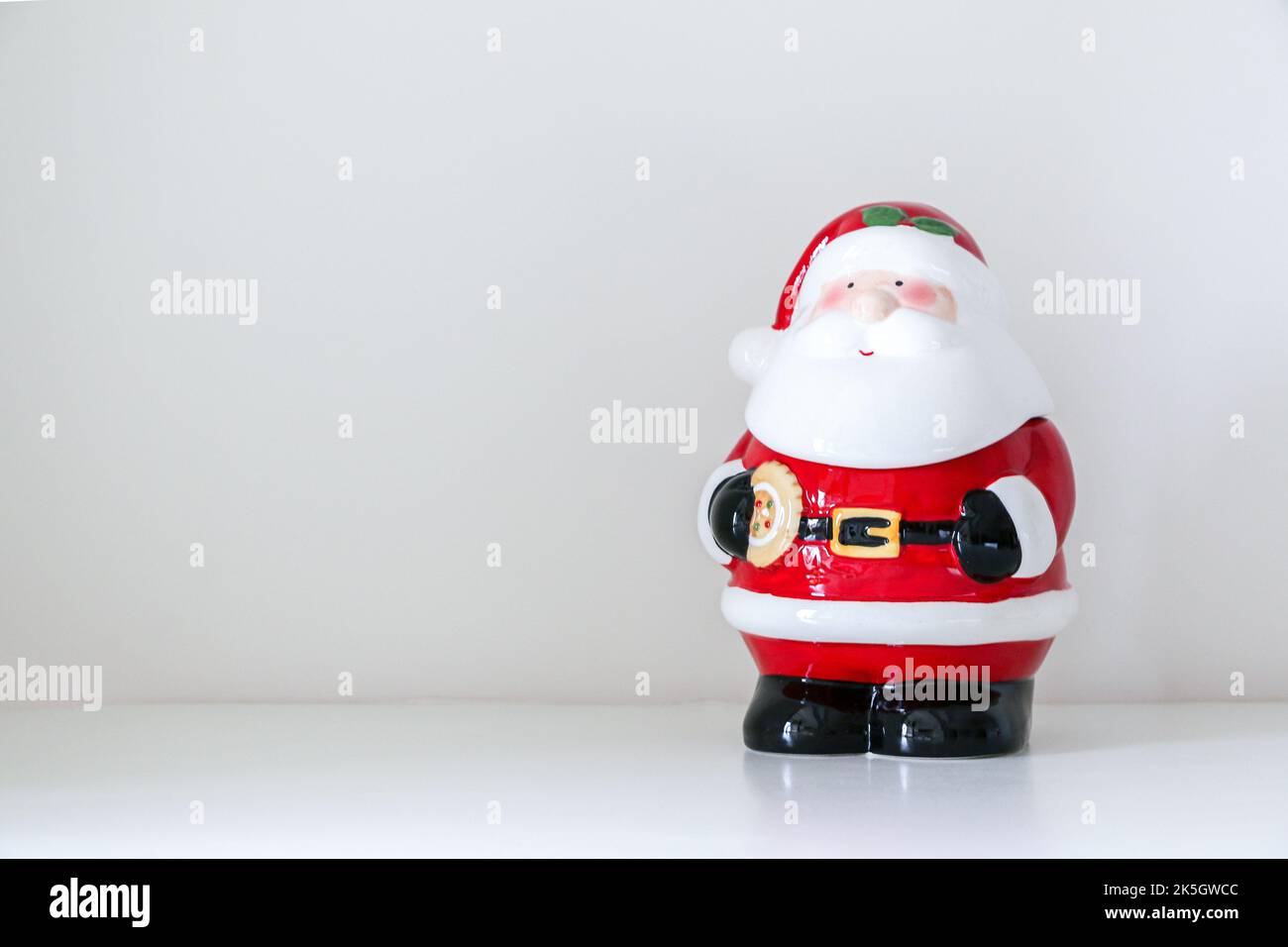 Natale Babbo Natale figurina in piedi inclinato a sinistra decorando bianco sfondo innevato di casa interna, copia spazio a sinistra Foto Stock