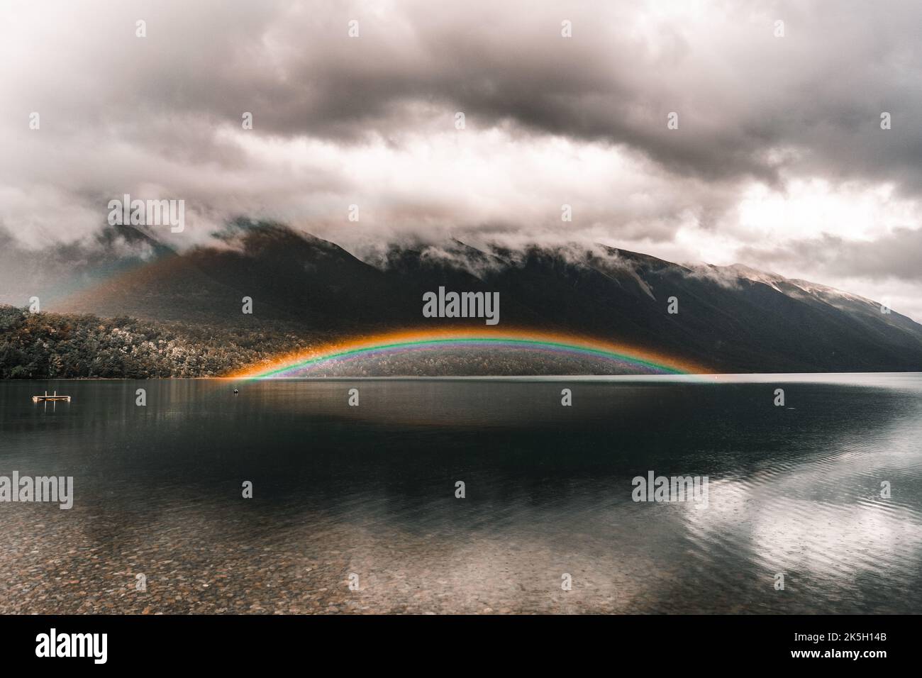 spettacolare e curioso arcobaleno luminoso sulle acque del tranquillo lago trasparente con fondo di pietre e rocce in un ambiente molto naturale Foto Stock