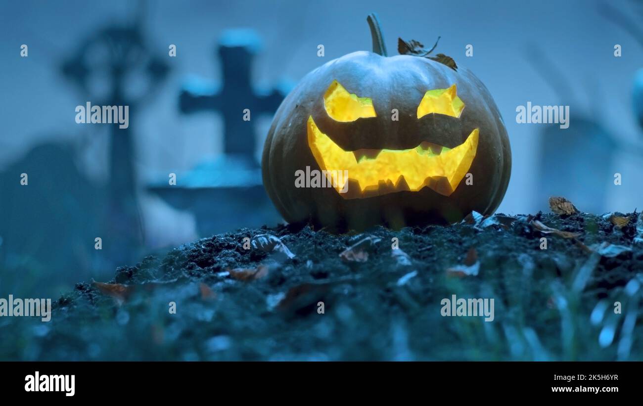 Zucca di Halloween incandescente tra le tombe del cimitero. Evento di festa Halloween concetto. Foto Stock