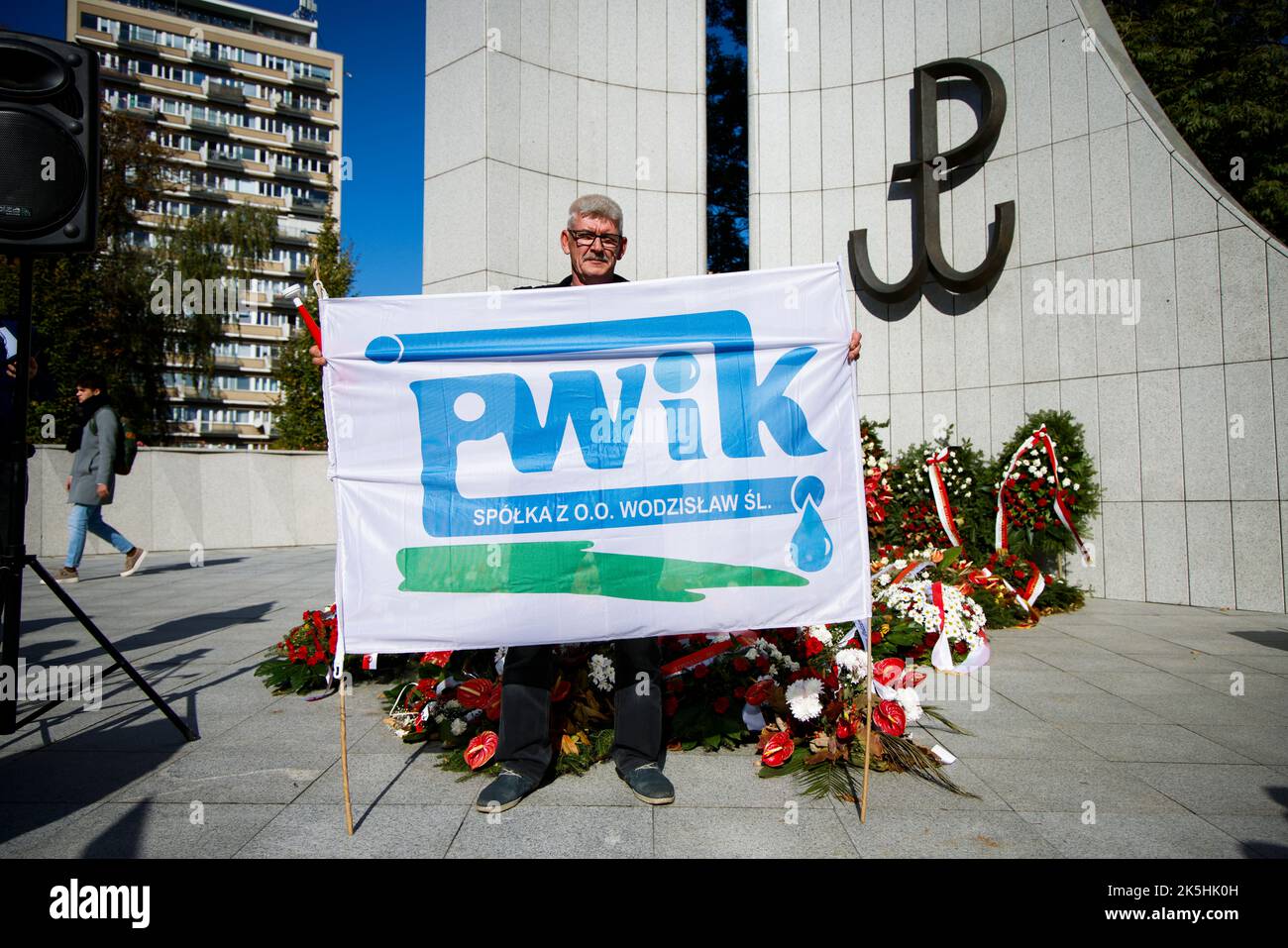Un uomo che regge uno striscione con il logo di un impianto locale di trattamento delle acque di Wodzislaw è visto di fronte al monumento del secondo mondo polacco W. Foto Stock