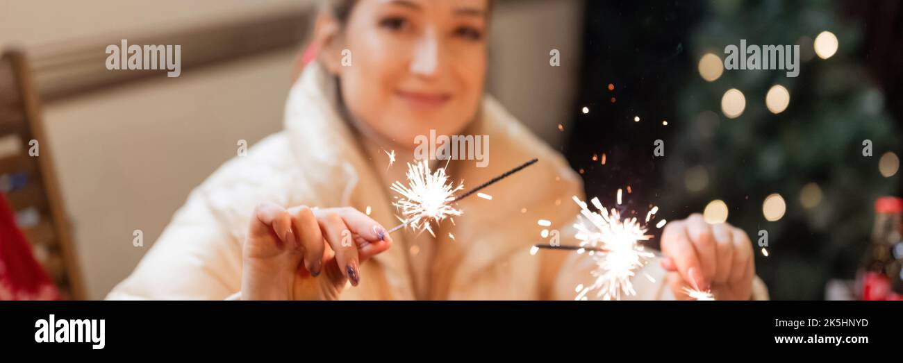 giovane donna sfuocata che tiene in mano sparklers fuoco bengala bastoni con una tela rossa all'aperto su felice anno nuovo e buon natale vacanza invernale Foto Stock
