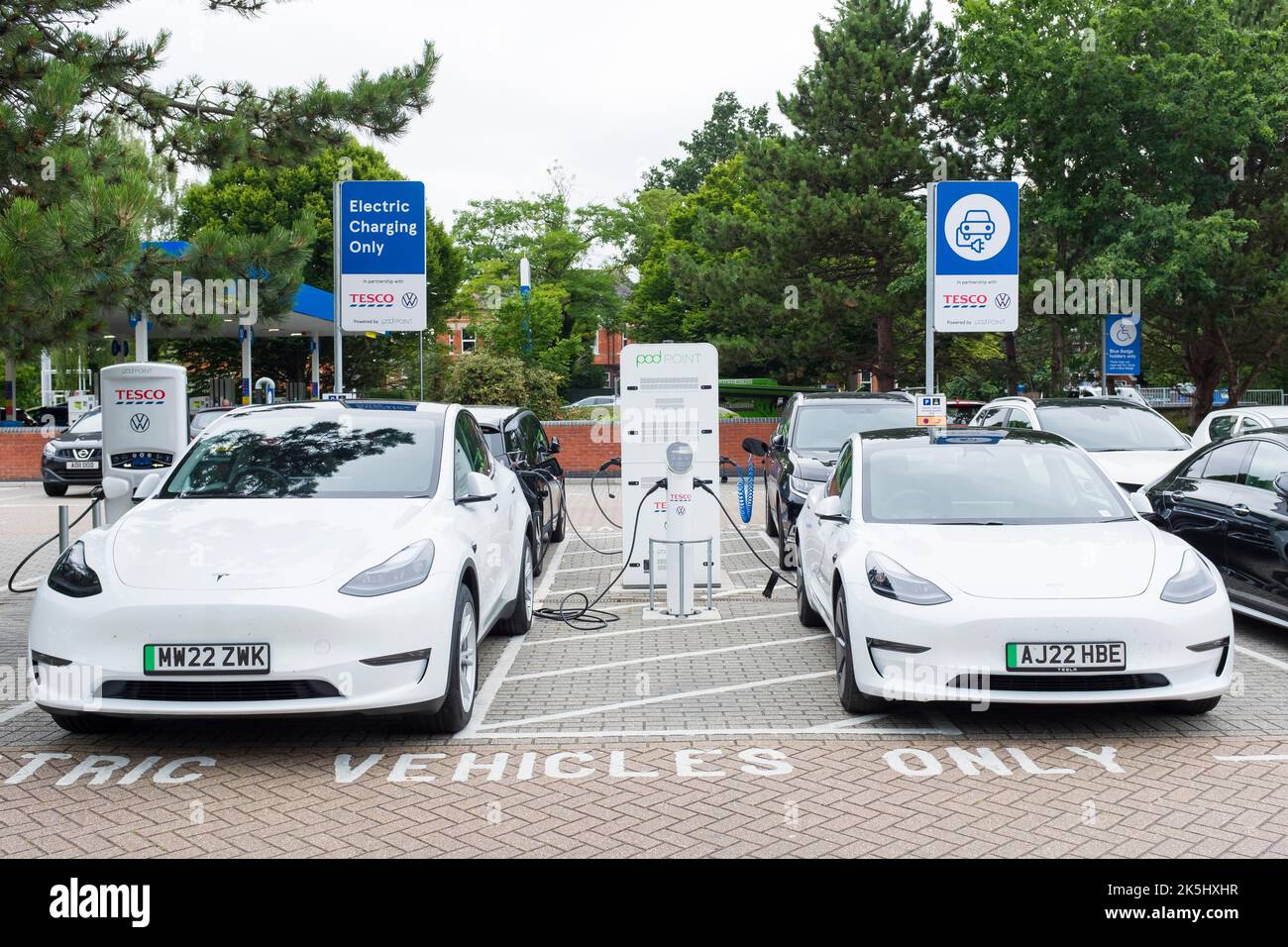 POOLE, Regno Unito - 07 luglio 2022. Due auto Tesla EV bianche si ricaricano presso una stazione di ricarica per auto elettriche in un parcheggio Tesco Foto Stock