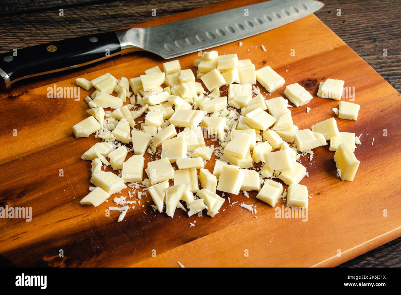 Cioccolato bianco tagliato su un tagliere di legno: Pezzi di cioccolato bianco con un coltello da cucina su un tagliere di legno Foto Stock
