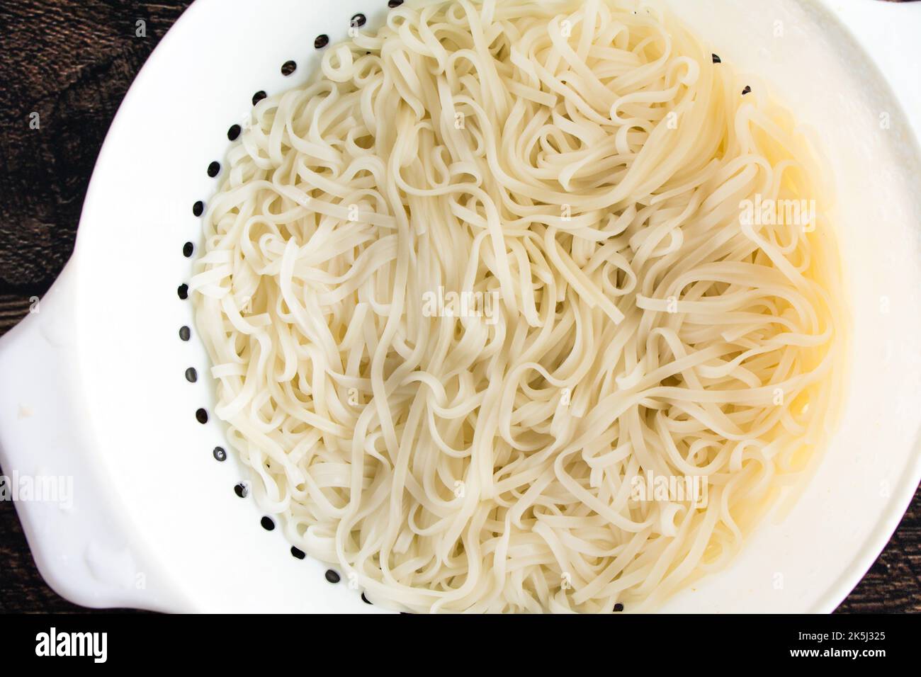 Tagliatelle di riso cotte e sgocciolate in un colapasta di plastica bianca: Vista dall'alto di tagliatelle cotte in un setaccio Foto Stock