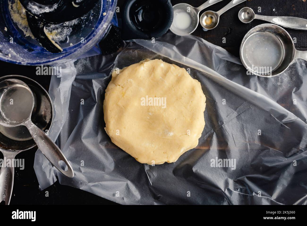 Pasta crosta crostata su un pezzo di plastica Wrap: Pasta sfoglia cruda formata a forma di disco circondato da utensili da cucina Foto Stock