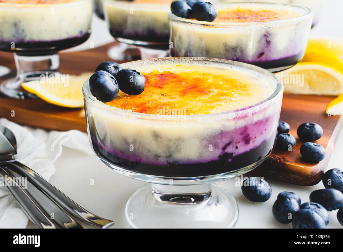 Mirtillo-arancia Creme Brulee guarnito con mirtilli freschi: Vista laterale della crema su confettura di mirtilli ricoperta di zucchero caramellato Foto Stock