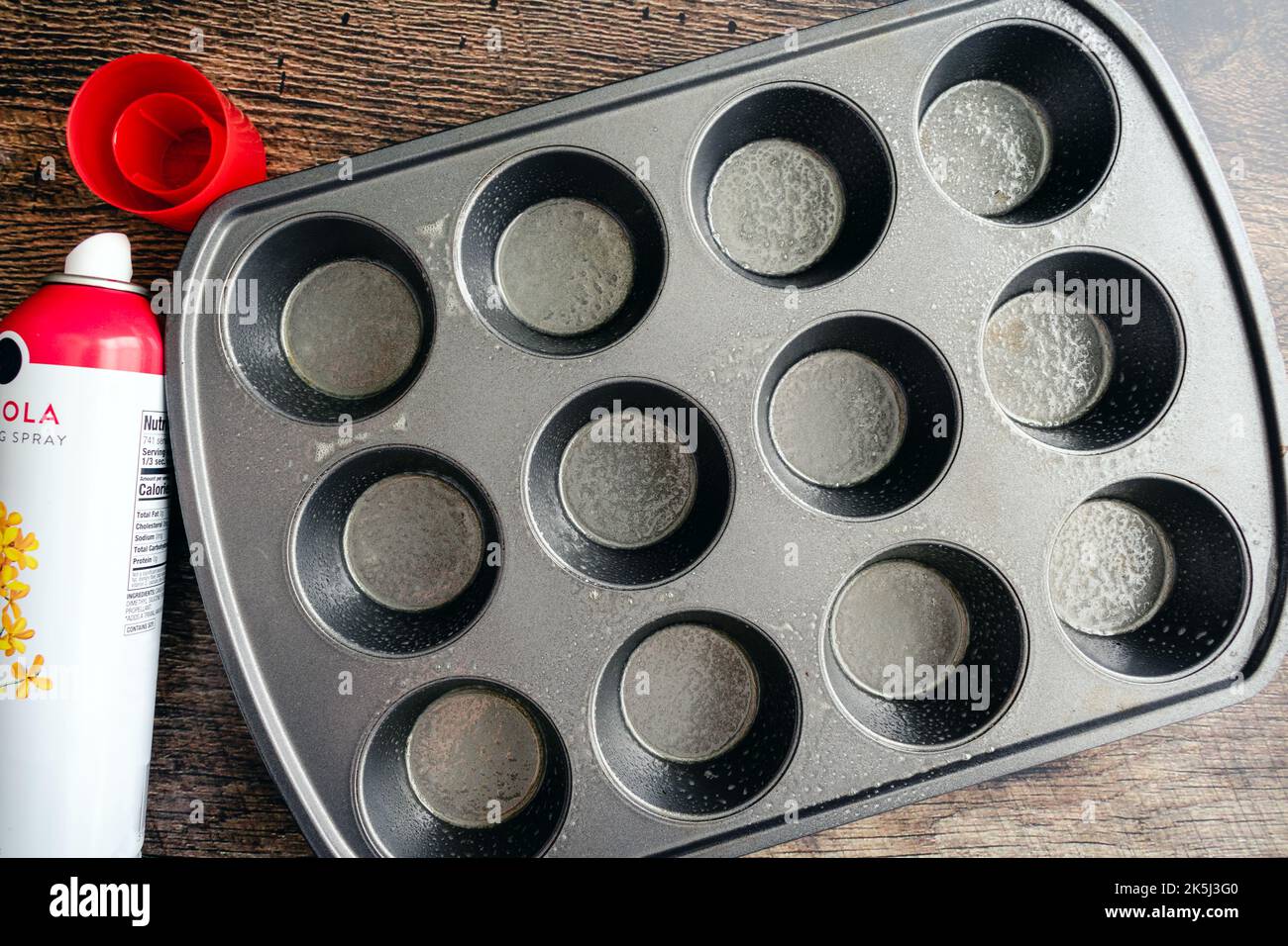 Teglia antiaderente per muffin in metallo spruzzata con olio di canola: Teglia antiaderente lubrificata con una bomboletta spray di spray da cucina Foto Stock Teglia antiaderente per muffin in metallo spruzzata con olio di canola: Teglia antiaderente lubrificata con una bomboletta spray di spray da cucina Foto Stock