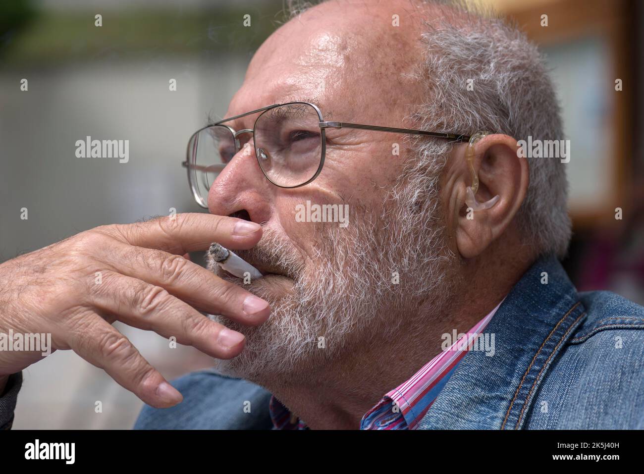 Ritratto di un Signore fumatore con barba e apparecchi acustici in orecchio, Baviera, Germania Foto Stock