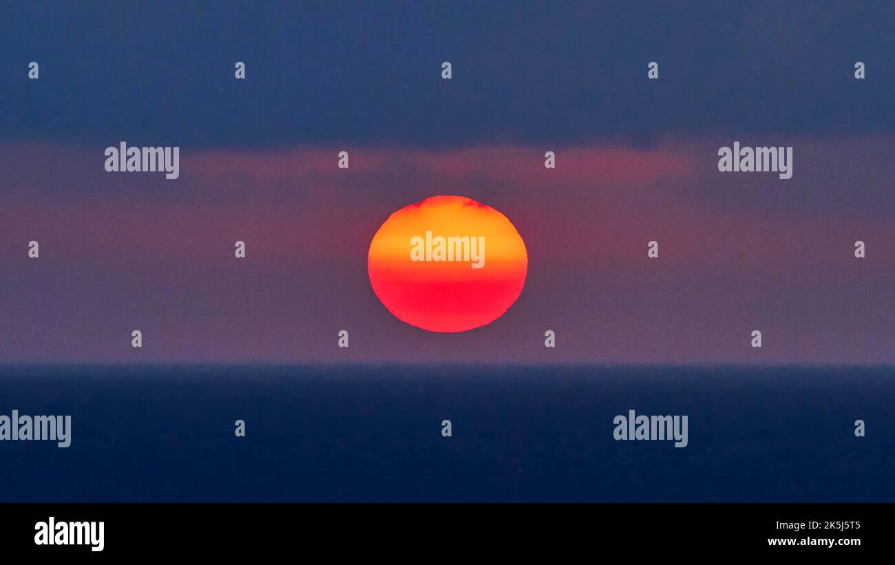 Sole come una grande palla rossa ardente, cielo blu-viola, sole appena sopra l'orizzonte, tramonto, luce serale, penisola Rodopou, penisola di Gramvoussa, Creta ovest Foto Stock