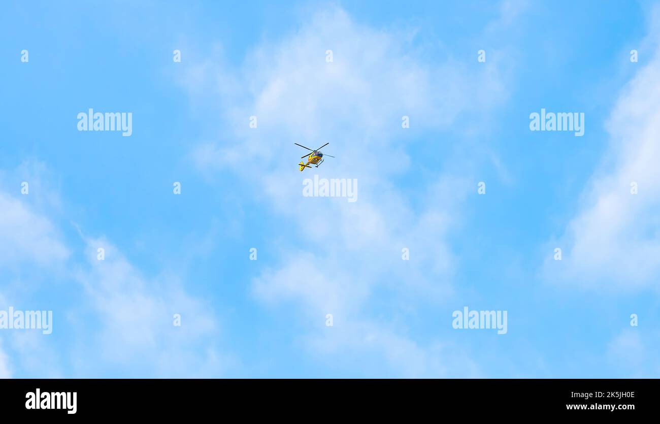 Un elicottero giallo vola in alto nel cielo blu chiaro. Foto Stock