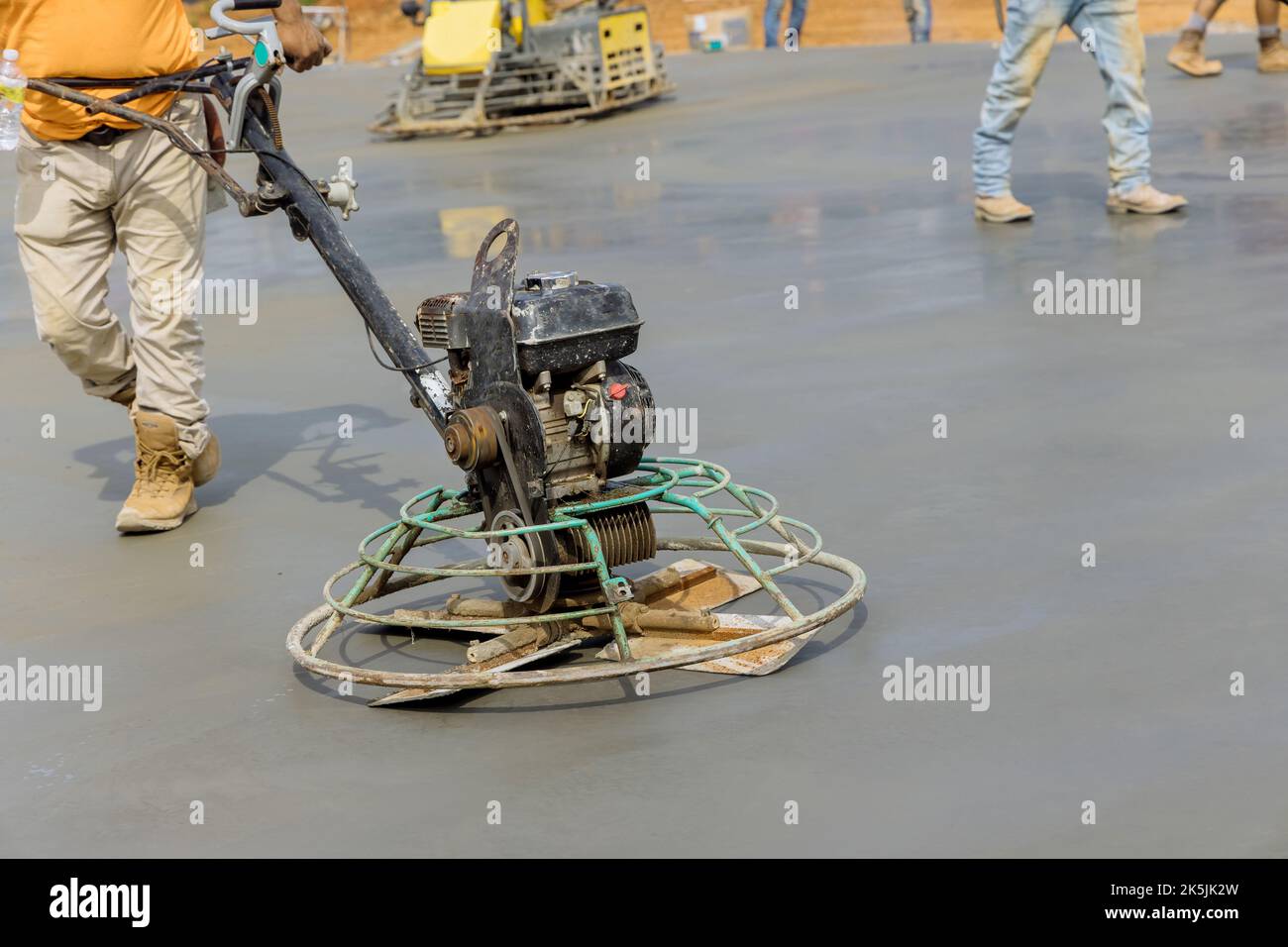 In cantiere, il lavoratore lucida e livella il pavimento in Malta del massetto di cemento come parte del processo di costruzione Foto Stock